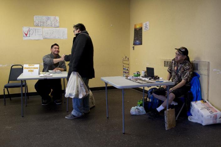 In this Oct. 8, 2014 photo, manning an informational table at the entrance of the main general store in Barrow, Alaska, Gabe Tegoseak, left, meets a friend as he sits below handmade signs reading “Are you a whaler?” and “Vote Early.” With much of the townspeople at the beach celebrating the catch of another whale, he&#39;s prepared for a light crowd. Tegoseak is working the ground game for Democratic Sen. Mark Begich. (AP Photo/Gregory Bull)