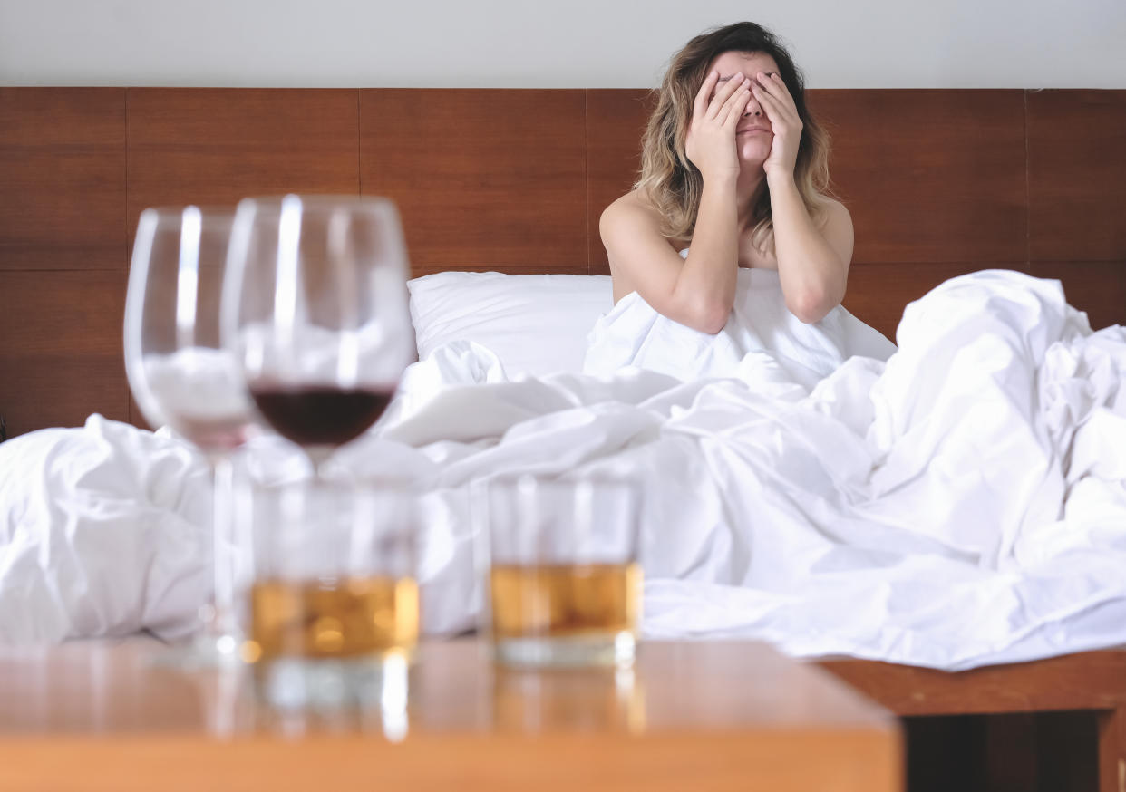 Woman with a hangover in bed with glasses of alcohol around her. (Getty Images)