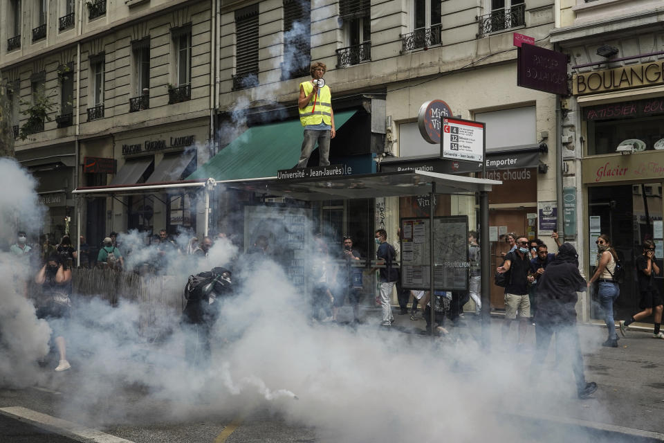 Protestors stand in smoke flares in front of policemen during a demonstration in Lyon, central France, Saturday, July 31, 2021. Demonstrators gathered in several cities in France on Saturday to protest against the COVID-19 pass, which grants vaccinated individuals greater ease of access to venues. (AP Photo/Laurent Cipriani)