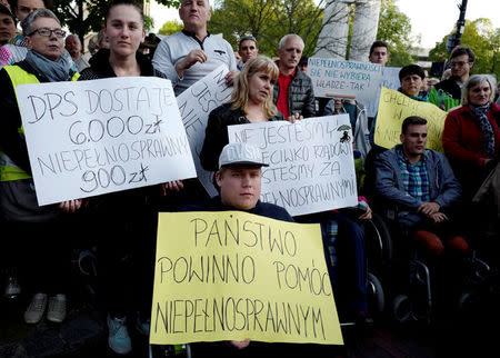 FILE PHOTO: People gather outside of the Parliament building to support the disabled people and caretakers who protest inside, demanding higher allowances, in Warsaw, Poland April 27, 2018. The banner reads "State should help disabled people". REUTERS/Kacper Pempel/File Photo