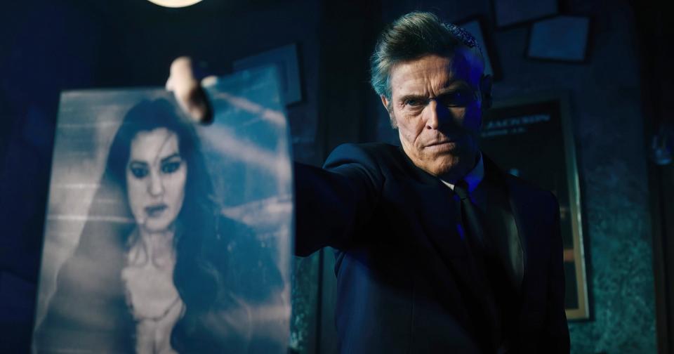 Willem Dafoe, dressed in a dark suit, holds up a photograph of a desperate woman (Monica Bellucci) in a dramatic scene that probably comes from a TV show or movie