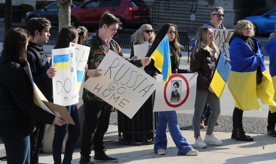 The flag of Ukraine and messages targeting Russian President Vladimir Putin and Russia are held by participants during a rally against the invasion of Ukraine, Saturday, March 5, 2022, at Wilmington's Rodney Square.