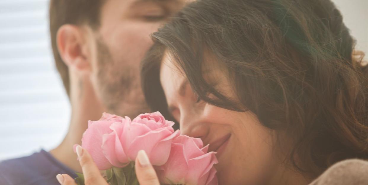 adult man and woman with bouquet of pink roses sharing what looks like a romantic moment