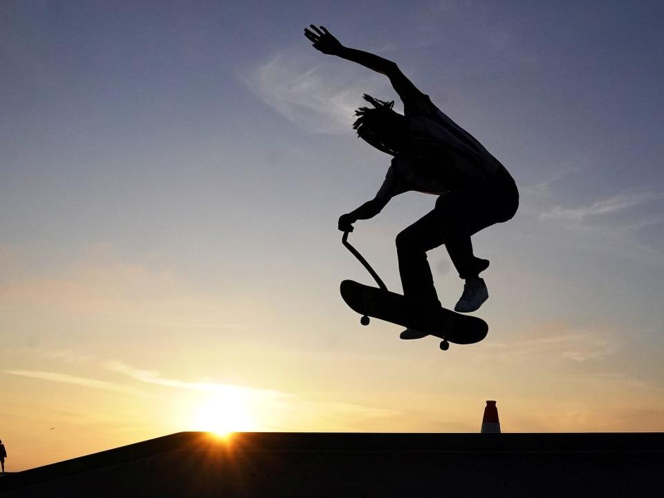 silhouette on skateboard jumps through the air against blue sky sunset