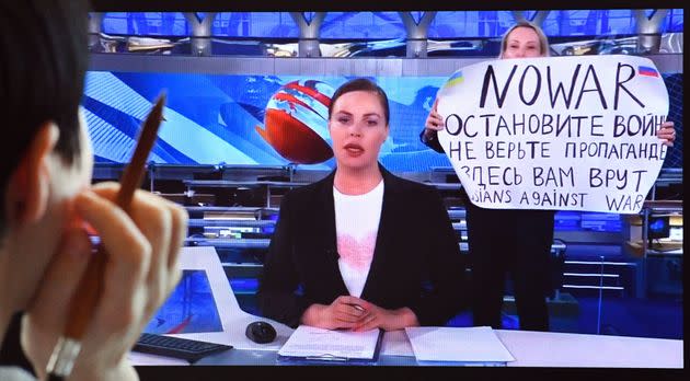 A woman looks at a computer screen watching a dissenting Russian Channel One employee entering an on-air TV studio during Russia's most-watched evening news broadcast, holding up a poster that reads 