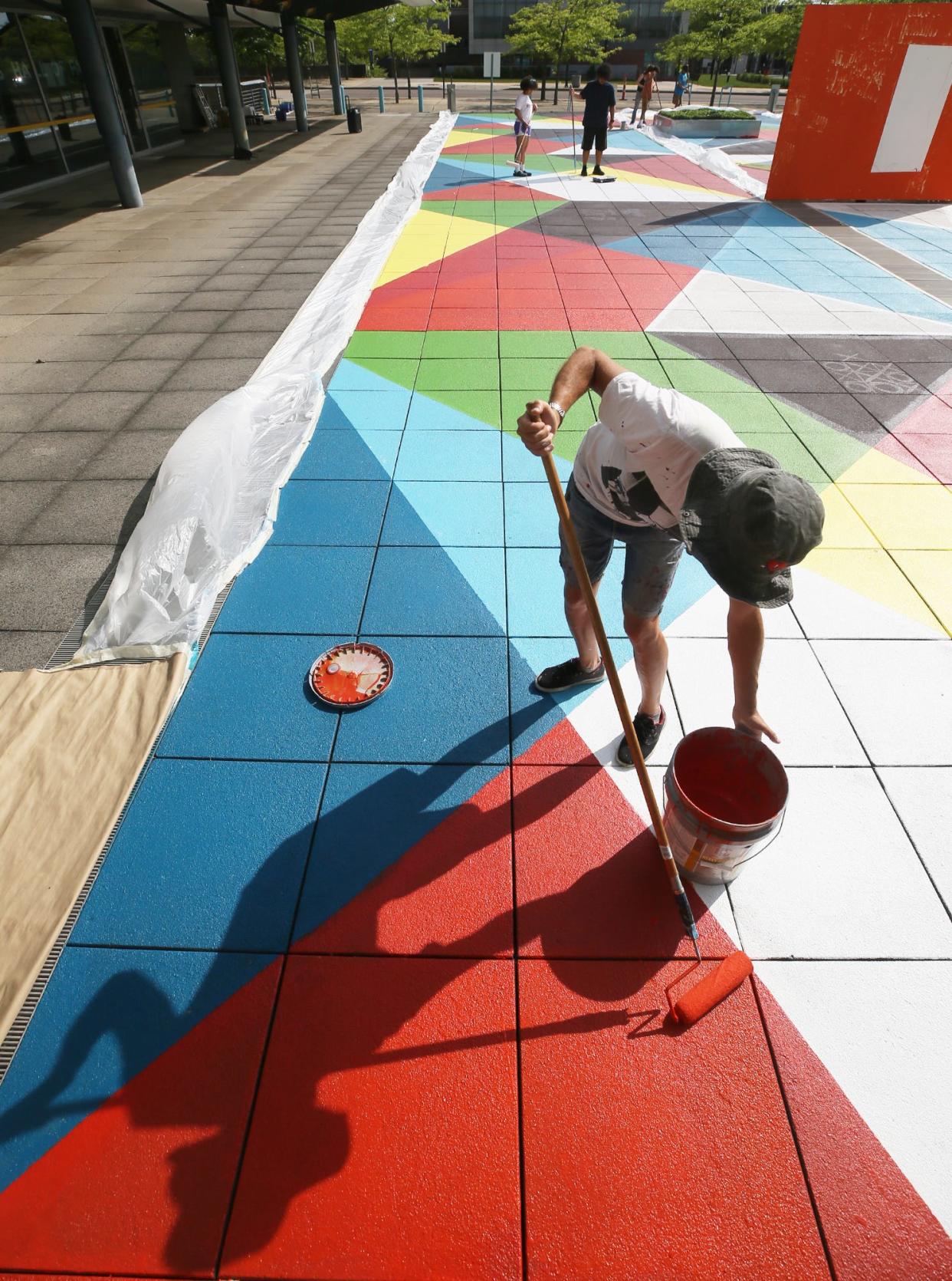 Jorge Munoz, an artist with Boa Mistura, works Monday on refreshing the paint on the STEM Plaza in Akron.