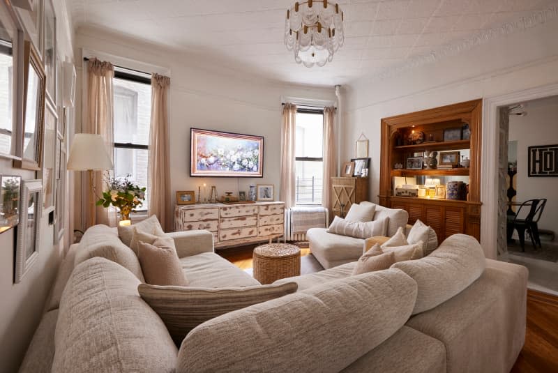 Sectional sofa in white living room with wood built-in unit and art frame TV hung above distressed dresser.