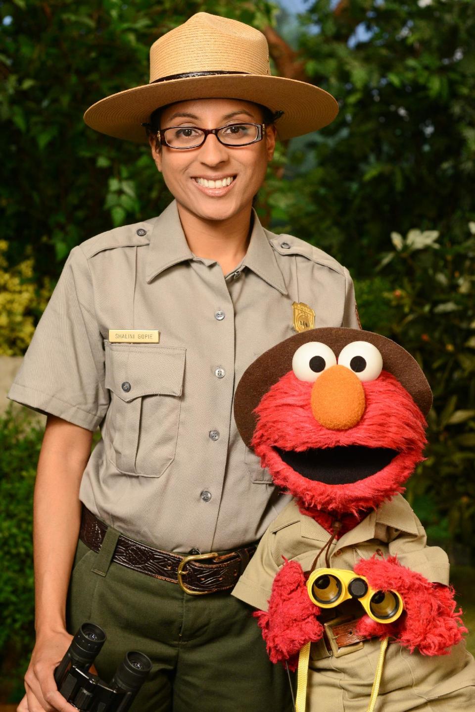 This undated publicity image released by Sesame Workshop shows Ranger Shalini Gopie with the character Elmo from the children's series "Sesame Street," during a segment on national parks. A new project has recruited Muppet monsters Elmo and Murray to visit national parks in six short videos that encourage children aged 3 through 5 to experience the great outdoors, wherever it might be, and to apply scientific skills of inquiry to learn about these natural settings. (AP Photo/Sesame Workshop)