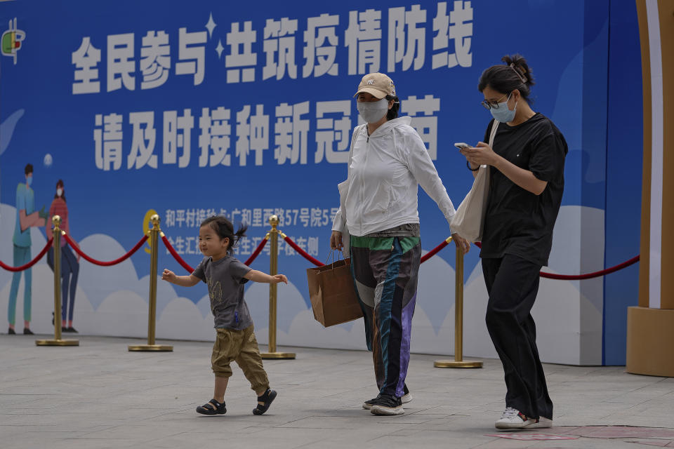 Women wearing face masks to help curb the spread of the coronavirus and a child walk by a billboard showing the words "All people participate in building a line of defense against the epidemic, please get the vaccine in time" on display outside a shopping mall in Beijing on May 24, 2021. If China is to meet its tentative goal of vaccinating 80% of its population against the coronavirus by the end of the year, tens of millions of children may have to start rolling up their sleeves. (AP Photo/Andy Wong)