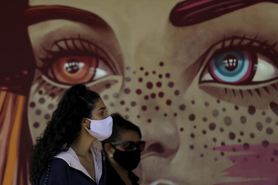 Women wear face masks amid the new coronavirus pandemic as they wait for a quick test at a COVID-19 testing site set up on a public school's basketball court in the Estrutural neighborhood of Brasilia, Brazil, Tuesday, May 26, 2020. According to officials, the objective is to expand surveillance and the tracking of possible asymptomatic positive cases, especially in poor, remote areas. (AP Photo/Eraldo Peres)