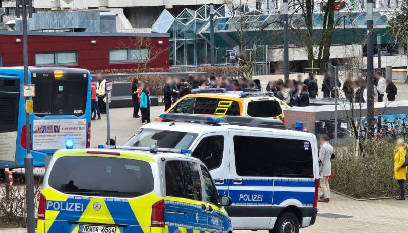 Police vehicles, pupils and other people stand in front of a school. Several pupils have been injured at a school in Wuppertal. A suspect has been arrested, said a police spokesman in Düsseldorf. The police are on the scene with strong forces. -/Pressefoto Otte/dpa