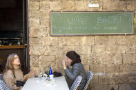 Women sit in a restaurant as restrictions are eased following months of government-imposed shutdowns, in Tel Aviv, Israel, Sunday, March 7, 2021. Israel reopened most of its economy Sunday as part of its final phase of lifting coronavirus lockdown restrictions, some of them in place since September. The sign says you'r invited for amazing food and cold beer. (AP Photo/Ariel Schalit)