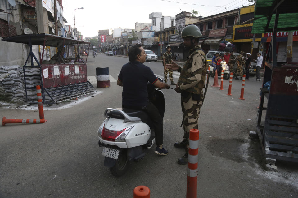 An Indian paramilitary soldier stops a commuter during curfew like restrictions in Jammu, India, Monday, Aug. 5, 2019. An indefinite security lockdown was in place in the Indian-controlled portion of divided Kashmir on Monday, stranding millions in their homes as authorities also suspended some internet services and deployed thousands of fresh troops around the increasingly tense region. (AP Photo/Channi Anand)