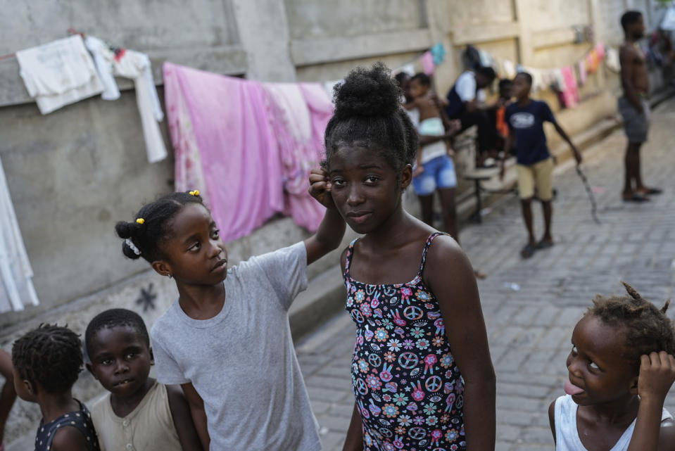 Juliana St. Vil, center, stands inside a school converted into a shelter where she now lives, after fleeing gang violence in her neighborhood, in Port-au-Prince, Haiti, Saturday, May 18, 2024. The 12-year-old now sleeps on the concrete floor, living in a classroom with nearly a dozen strangers, sharing a handful of bathrooms with more than 2,200 people. (AP Photo/Ramon Espinosa)