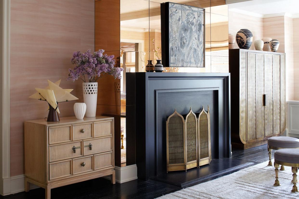black fireplace with minaret shaped tops against a mirrored wall and next to a tall cabinet on one side and short chest on the other