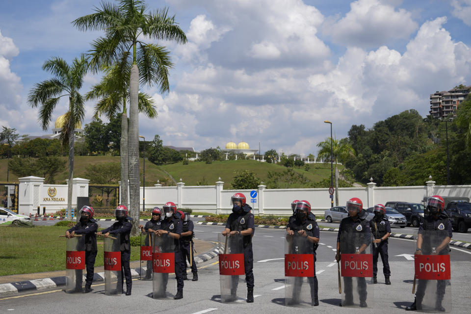 Police with riot shield stand guard as supporters of Malaysia's former Prime Minister Najib Razak gather outside the National Palace in Kuala Lumpur, Malaysia, Wednesday, Aug. 24, 2022. They gathered to seek royal intervention just a day after Najib began a 12-year jail term, while opponents launched an online petition urging the monarch to deny clemency. (AP Photo/Vincent Thian)
