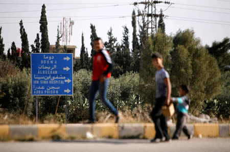 People walk next to a road sign at Wafideen camp in Damascus, Syria April 1, 2018. REUTERS/Omar Sanadiki