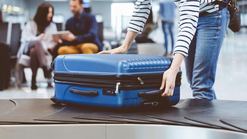 Young woman passenger collecting her luggage from conveyor belt.