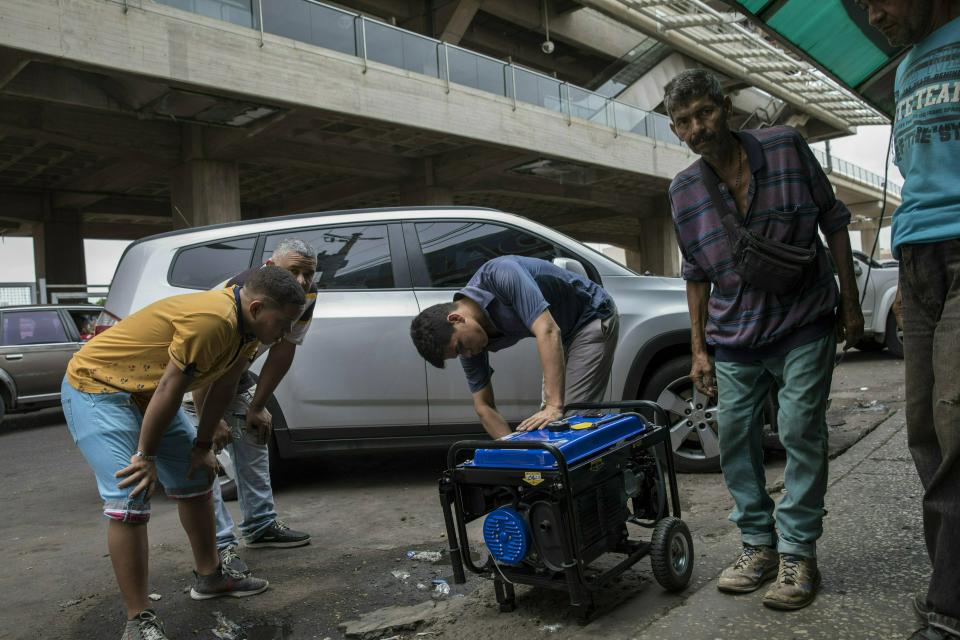 In this May 23, 2019 photo, a vendor shows a power generator to customers at the Maracaibo flea marker, in Venezuela. Millions of poor live at the mercy of Venezuela's unstable power grid, but middle- and upper-class residents able to scrape together enough dollars are buying backup generators in an attempt to regain a normal life. (AP Photo/Rodrigo Abd)