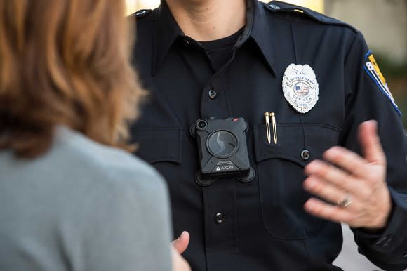 Police officer in uniform wearing Axon body camera while talking with someone.