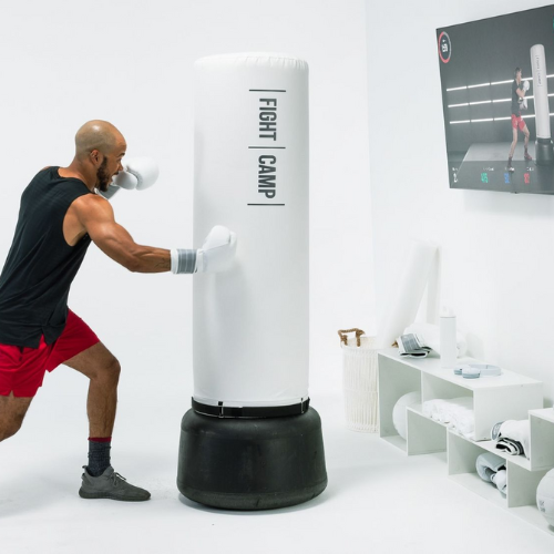 man boxing using FightCamp punching bag and following instructor on TV