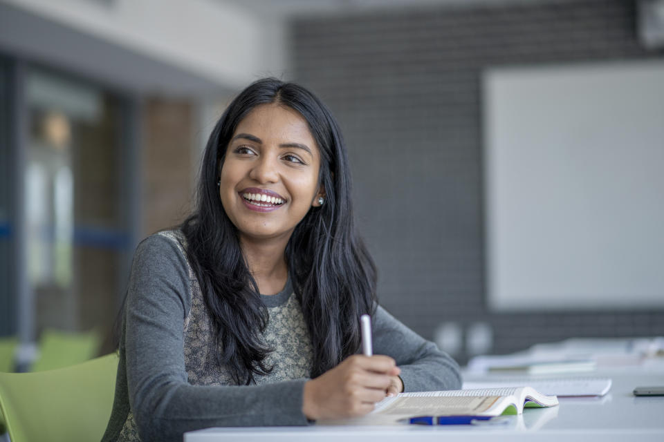 A girl happily sitting in front of a book with a pen in her hand