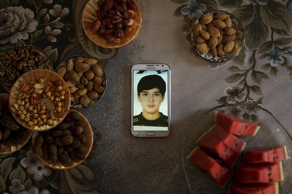 In this Aug. 24, 2018, photo, a phone displaying an image of Pakzat Qurban, now 18, who was imprisoned in China when he was 16, sits on a table surrounded with plates of watermelon and nuts at the home of his parents in Istanbul, Turkey. Qurban and his family moved to Turkey from in 2015, and Qurban was arrested at a Chinese airport when he went back to visit his grandparents. His parents, Qurbanjan Nurmemet and Gulgine Mehmut, say they received an 8 second video from an officer of their son strapped to a torture chair to try to coerce them to spy for Chinese police. (AP Photo/Dake Kang)