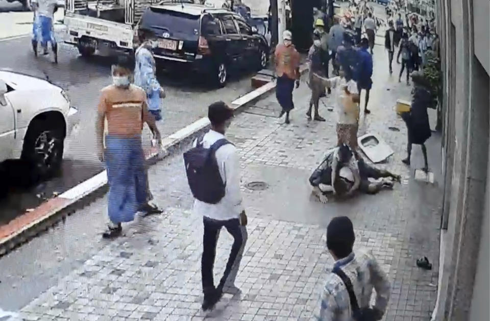 In this image taken from video obtained by Than Lwin Khet News, a woman helps an unidentified man lying on the sidewalk of Sule Pagoda Road after he was attacked by a group of men in Yangon, Myanmar, Thursday, Feb. 25, 2021. Members of a group supporting Myanmar's military junta have attacked and injured people protesting against the army’s Feb. 1 seizure of power that ousted the elected government of Aung San Suu Kyi. (Than Lwin Thet News via AP)