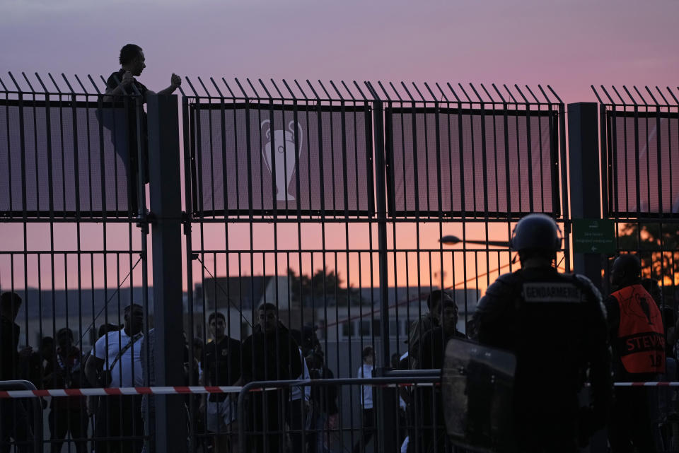 A fan stands on the fence in front of the Stade de France prior the Champions League final soccer match between Liverpool and Real Madrid, in Saint Denis near Paris, Saturday, May 28, 2022. Police have deployed tear gas on supporters waiting in long lines to get into the Stade de France for the Champions League final between Liverpool and Real Madrid that was delayed by 37 minutes while security struggled to cope with the vast crowd and fans climbing over fences. (AP Photo/Christophe Ena)