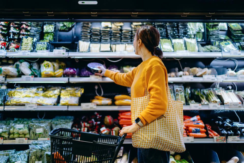 Person shopping in grocery store, selecting produce, with basket