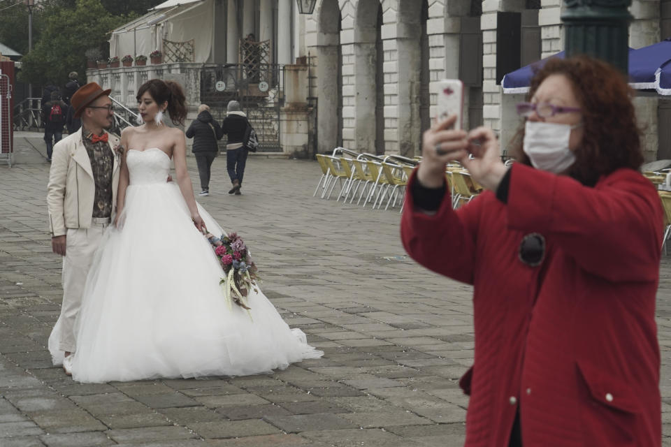 A newlywed couple pose for photos as tourists wear protective masks in Venice, Italy, Tuesday, Feb. 25, 2020. Italy has been scrambling to check the spread of Europe's first major outbreak of the new viral disease amid rapidly rising numbers of infections and calling off the popular Venice Carnival and closing tourist attractions.(AP Photo/Renata Brito)