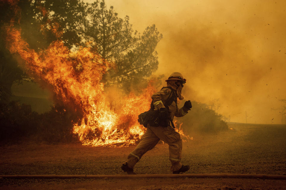 FILE - In this July 31, 2018, file photo, a firefighter runs while trying to save a home as a wildfire tears through Lakeport, Calif. While California officials quickly determined an arsonist started the wildfire burning southeast of Los Angeles and that sparks from a vehicle produced the deadly wildfire in the city of Redding, causes for many of the state's worst blazes in the past decade remain a mystery. (AP Photo/Noah Berger, File)