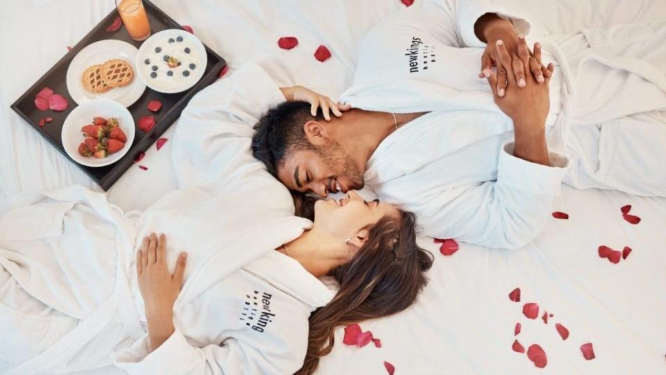Young couple on bed, with flower petals and healthy snack on tray while on holiday