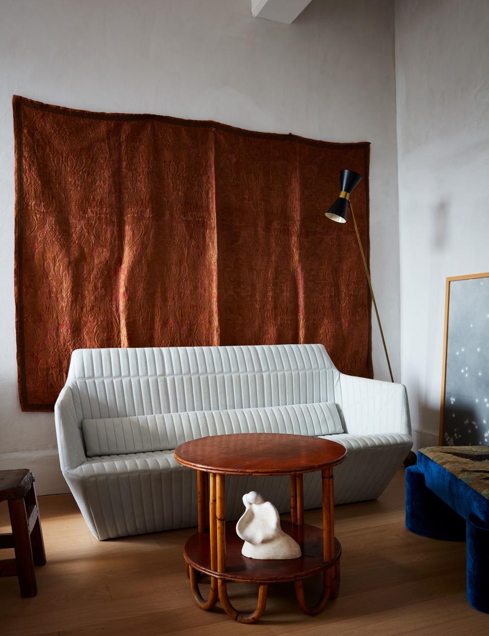 In the bedroom sitting area, an 18th century Italian silk tapestry hangs behind a Facett sofa by Ronan and Erwan Bouroullec for Ligne Roset, a vintage bamboo side table, a tapestry-covered chair by Valle, a vintage Stilnovo lamp, and a painting by Katherine Keltner.