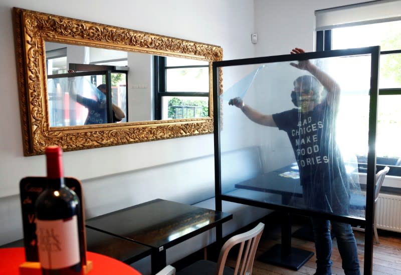 A worker installs a protective plexiglass barrier between the tables in a restaurant in Brussels