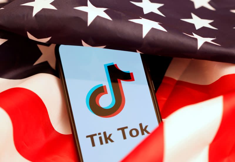 Tik Tok logo is displayed on the smartphone while standing on the U.S. flag in this illustration