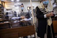 Ultra-Orthodox Jews wearing face masks during a morning prayer in a synagogue separated by plastic partitions, follow new government measures to help stop the spread of the coronavirus, in Bnei Brak, Israel, Friday, Sept 18, 2020. Israel is set to go back into a three-week lockdown later Friday to try to contain a coronavirus outbreak that has steadily worsened for months as its government has been plagued by indecision and infighting. (AP Photo/Oded Balilty)