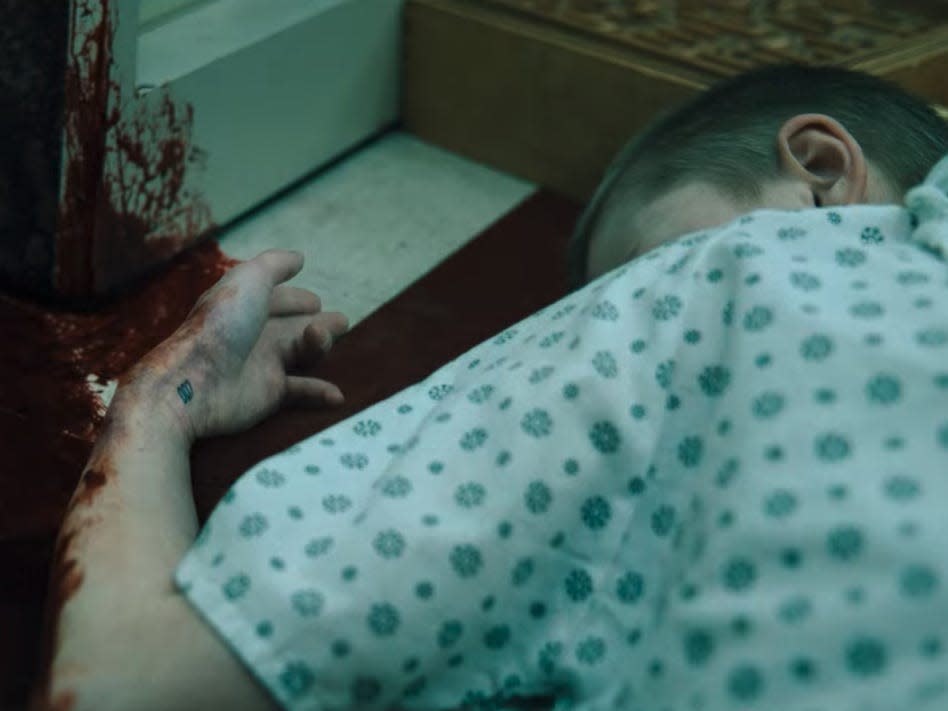 a child in stranger things laying in a pool of blood, completely unmoving and with a number tattooed on its wrist