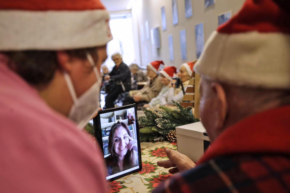 Giuseppe Vitali, right, is flanked by carer Melania Cavalieri as he talks on a video call with Manuela Diana, a donor, unrelated to him, who bought and sent him a Christmas present through an organization dubbed "Santa's Grandchildren", at the Martino Zanchi nursing home in Alzano Lombardo, one of the area that most suffered the first wave of COVID-19, in northern Italy, Saturday, Dec. 19, 2020. (AP Photo/Luca Bruno)