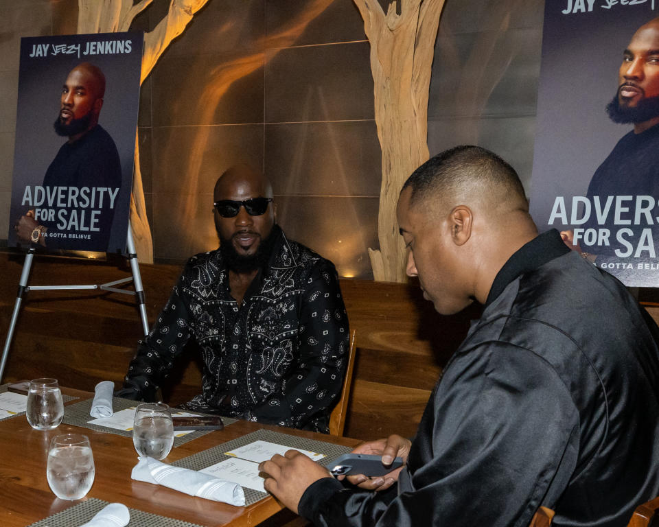 Jenkins sits at a dinner table, with posters on stands advertising his memoir nearby.