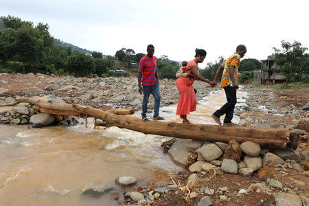 A man helps a woman cross a log bridge after the flash flood washed away a concrete bridge at Pentagon, in Freetown August 18, 2017. REUTERS/Afolabi Sotunde