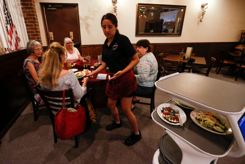 Server Alycia Alvaracdo takes food from a food server robot known as "Rosey" (right) at a table at Archie's Italian Eatery on East Republic Road on Tuesday, June 14, 2022.