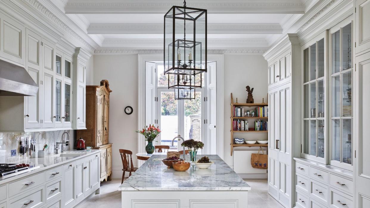  All white kitchen with kitchen island along the centre and metal frame rectangular lantern ceiling lights 