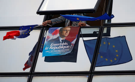 A supporter holds a campaign poster of Emmanuel Macron and European Union flags after results were announced in the second round of 2017 French presidential election at the campaign headquarters in Paris, France, May 7, 2017. REUTERS/Gonzalo Fuentes