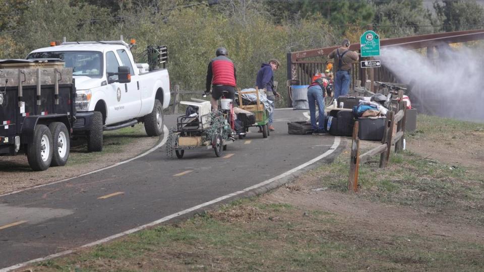 A city of San Luis Obispo worker powerwashes a pedestrian bridge on Bob Jones Trail near Prado Road while unhoused people who were living beside San Luis Obispo Creek tote their belongings away. The city cleared homeless camps along the trail ahead of a winter creek cleanup and fence construction project.