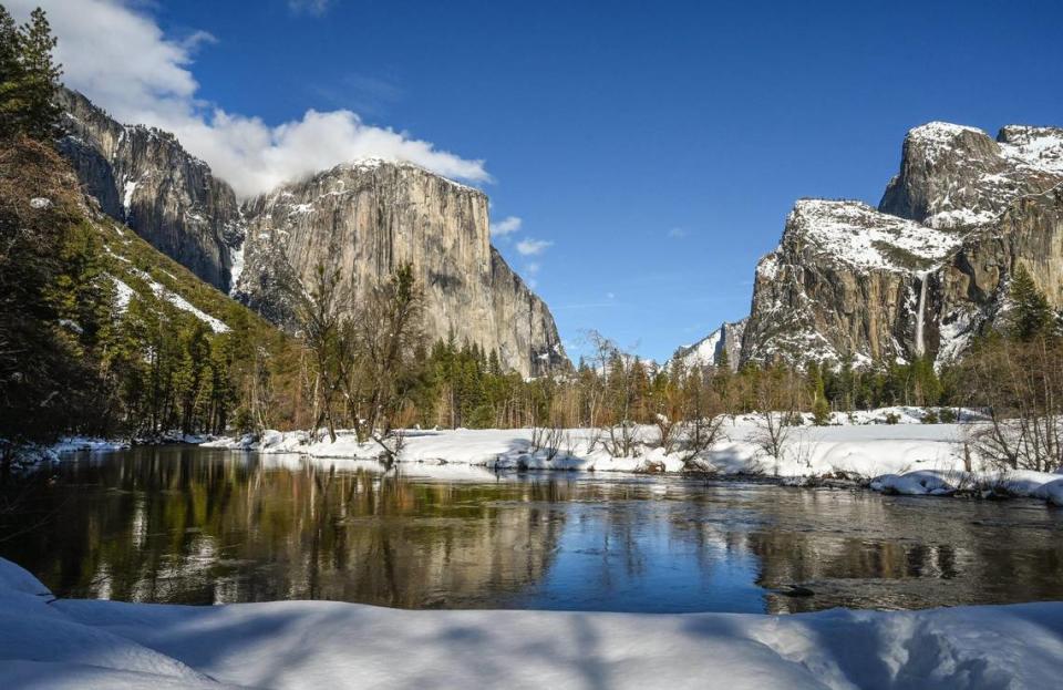 Clouds graze the top of El Capitan, left, as Bridalveil Fall, right, flows down into Yosemite Valley and the Merced River while a heavy blanket of snow covers the roadway banks on a rare day of no visitors on Friday, March 3, 2023. Park officials closed the entrances after recent snowstorms.