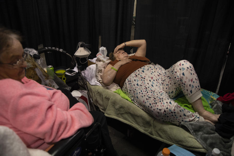 Sheryl Christian rests on a cot with her mother Pat Skundrick at the evacuation center set up at the Jackson County Fairgrounds on Saturday, Sept. 12, 2020 in Central Point, Ore. They lived together at the Glenwood Mobile park and lost their home to the destructive wildfires devastating the region. (AP Photo/Paula Bronstein)
