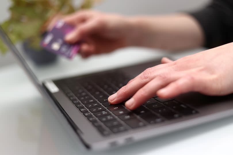 A woman uses a laptop as she holds a bank card