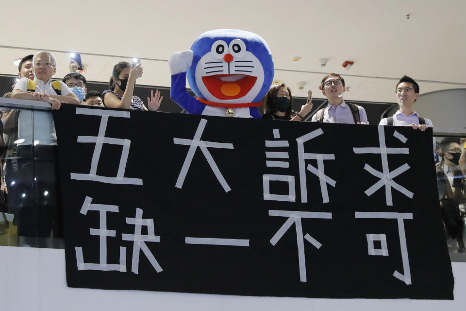 A man dressed as a cartoon character Doraemon, joins the demonstrators to sing a theme song written by protestors "Glory to Hong Kong" at the International Finance Centre (ifc) shopping mall in Hong Kong, Thursday, Sept. 12, 2019. Thousands of people belted out a new protest song at Hong Kong's shopping malls in an act of resistance that highlighted the creativity of demonstrators in their months-long fight for democratic freedoms in the semi-autonomous Chinese territory. The banner reads "Five demands - not one less." (AP Photo/Kin Cheung)