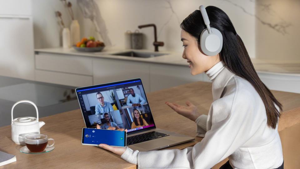 Girl wearing the Sony WH-1000XM5, holding a phone and looking at a laptop